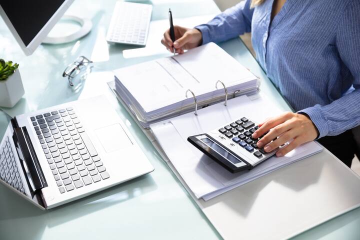 Businesswoman's Hand Calculating Bill With Calculator Over Desk In Office