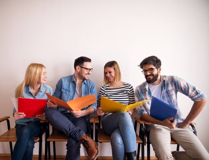 Several young and joyful businessmen are waiting for their opportunity to present their ideas safely placed in colorful folders.