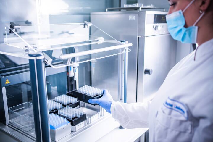 Female lab technician in a white coat and blue gloves conducting precise pipetting test in a pharmaceutical laboratory at Synergy Health Utrecht.