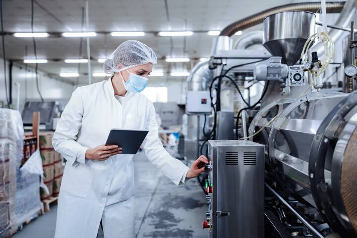 A female milk plant operator holding tablet and adjusting milk processing machine during corona virus.