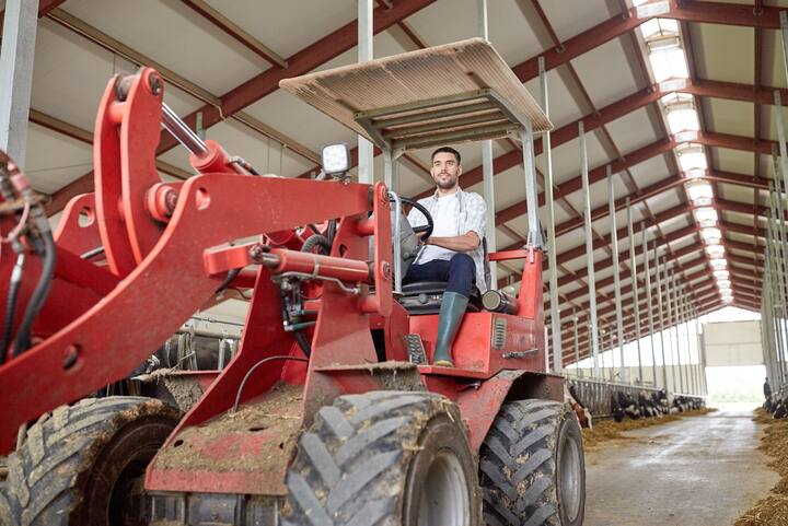 farming, agriculture and people concept - happy young man or farmer driving tractor at farm