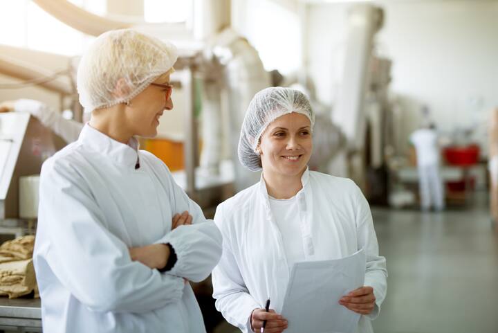 Two young gorgeous female workers are having a chat while one of them holds papers with statistics.