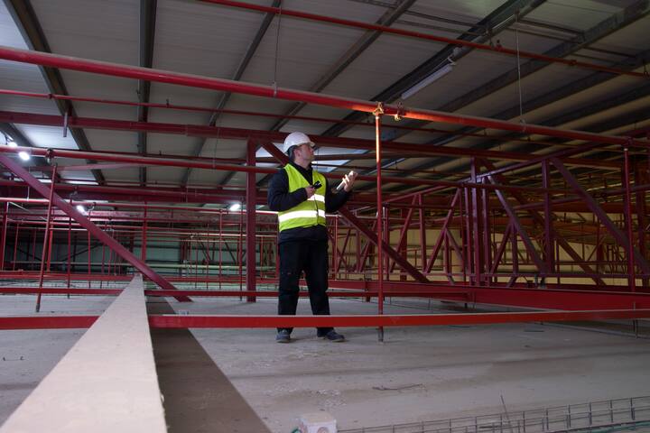 Technician engineer in a helmet checks the sprinklers pipes and roof constractions with a tablet