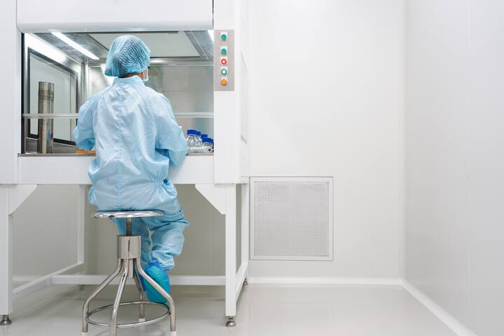 Unidentified microbiologist is testing the sample under the laminar air flow cabinet in the clean room of quality control laboratory in pharmaceutical industry.