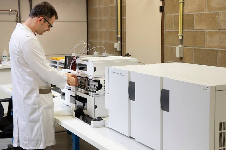Man in a lab coat operating an HPLC system (High Performance Liquid Chromatography) in a pharmaceutical laboratory setting.