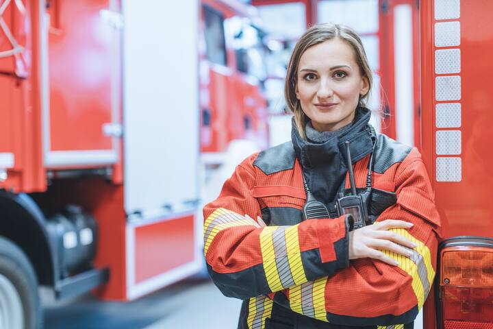 Fire fighter woman standing in front of a fire truck with her arms crossed
