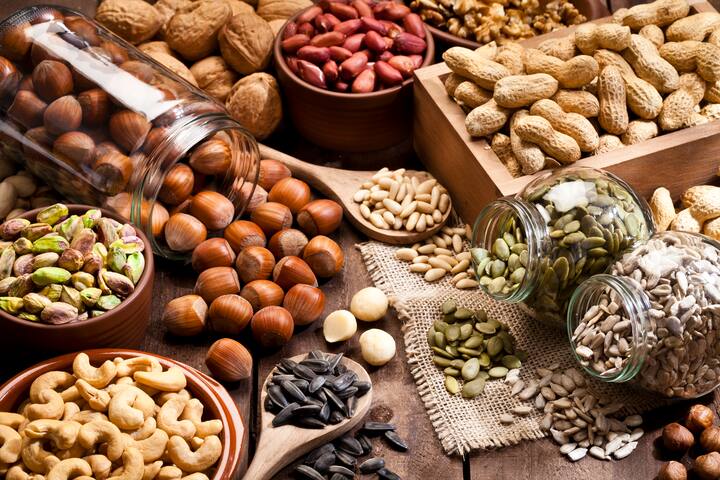 Horizontal shot of a rustic wood table filled with a large assortment of nuts like pistachios, hazelnut, pine nut, almonds, pumpkin seeds, sunflower seeds, peanuts, cashew and walnuts. Some nuts are in brown bowls and others in glass jars. Predominant color is brown. DSRL studio photo taken with Canon EOS 5D Mk II and Canon EF 100mm f/2.8L Macro IS USM