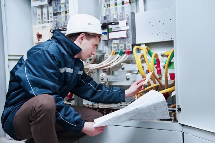 Electrician builder at work inspecting cabling connection of high voltage power electric line in industrial distribution fuseboard
