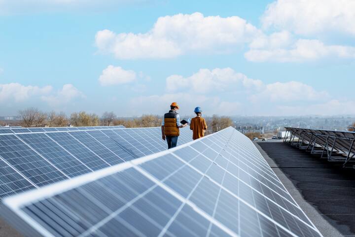 View on the rooftop solar power plant with two engineers walking and examining photovoltaic panels. Concept of alternative energy and its service