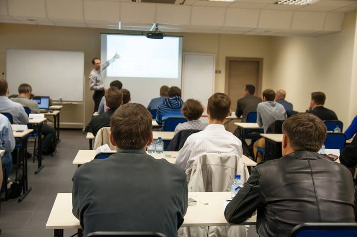 rear view of the people sitting in the class by the table and listening the presentation