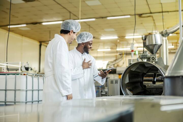 Smiling multicultural operators using tablet for operating machine and production line at food factory.
