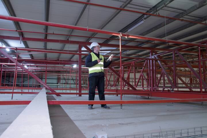 Technician engineer in a helmet checks the sprinklers pipes and roof constractions with a tablet