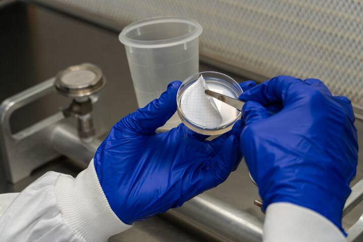 Gloved hands hold a small petri dish on which he places a membrane filter with tweezers