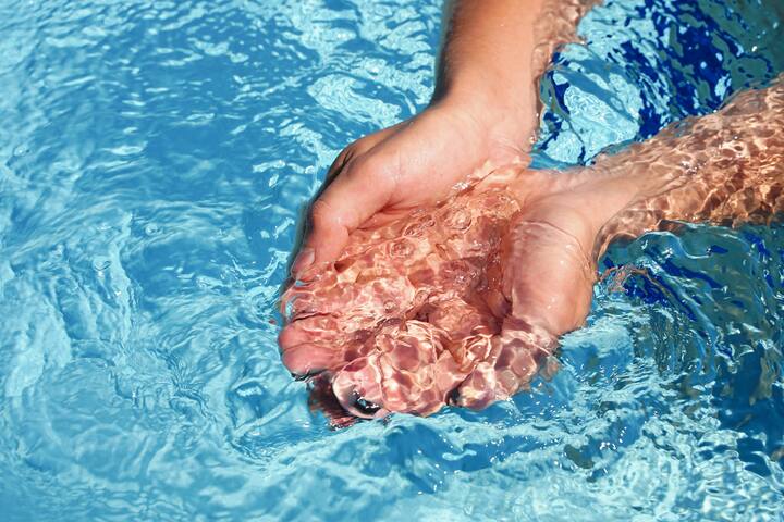 The hands cupped together submerged in clean clear blue water in swimming pool. High quality photo