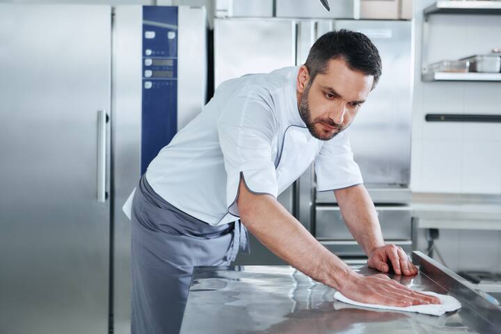 Bearded man prepares the surface for cooking in the kitchen. Cook carefully wipes the surface. Health and safety concept.