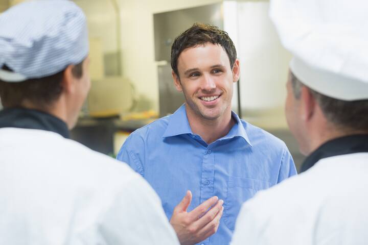 Young smiling manager talking to the staff standing in a kitchen