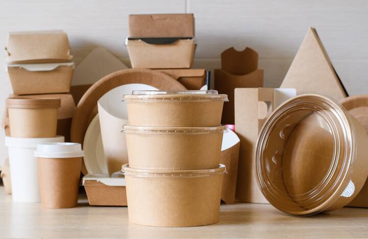 A set of round paper containers for food on the background of paper utensils and packaging. The concept of using dishes and packaging made from biodegradable environmentally friendly materials.