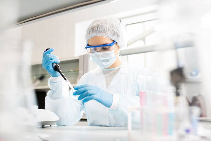 Female lab technician in protective clothing conducting precise pipetting test in a pharmaceutical laboratory for quality control