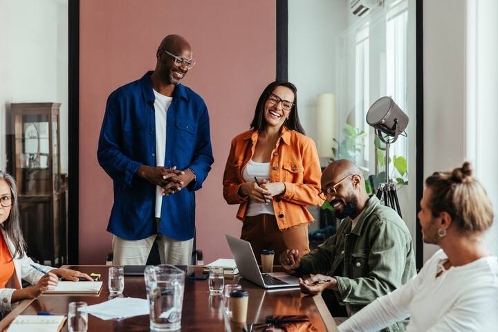 Co-workers in a relaxed boardroom meeting, collaborating and laughing. Modern space fosters teamwork and creativity.