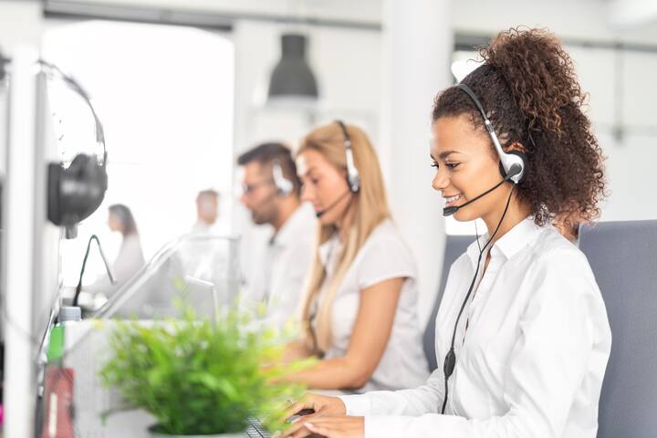 Call center worker accompanied by her team. Smiling customer support operator at work. Young employee working with a headset.