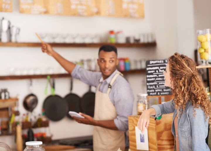 Woman, cafe and barista with pointing at menu for customer, purchase and decision in coffee shop. Waiter, small business and lady in restaurant with thinking, idea and choice for lunch order.
